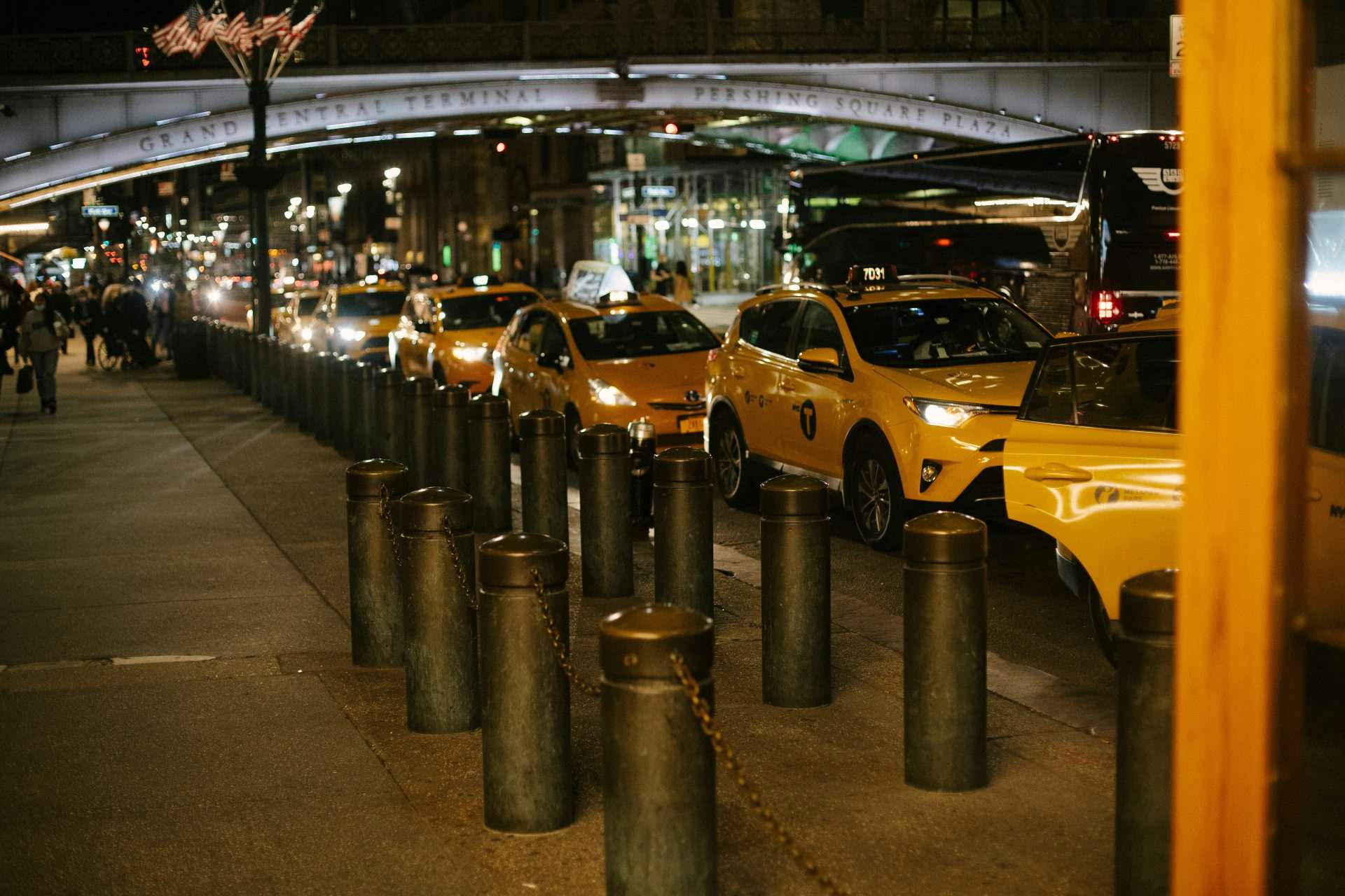 Fila de modernos taxis amarillos brillantes con faros brillantes estacionados al costado de la carretera cerca de Grand Central Terminal en Nueva York por la noche